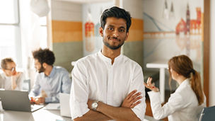 Smiling indian businessman standing in modern office on colleagues background