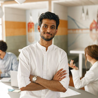 Smiling indian businessman standing in modern office on colleagues background