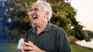 Senior man in aged care laughing outdoors in front of a tree