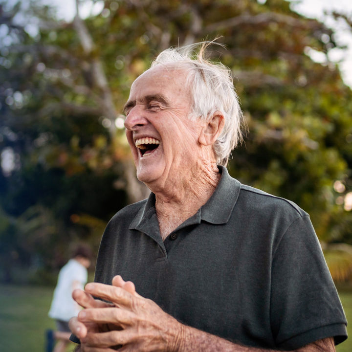 Senior man in aged care laughing outdoors in front of a tree