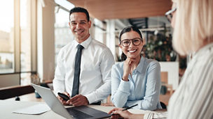 Smiling young businesswoman standing with two colleagues around a table during a meeting in a modern office