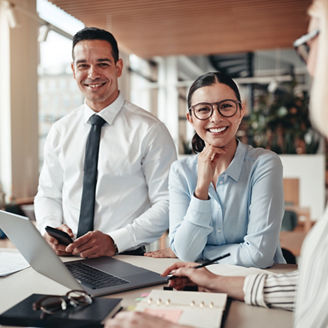Smiling young businesswoman standing with two colleagues around a table during a meeting in a modern office