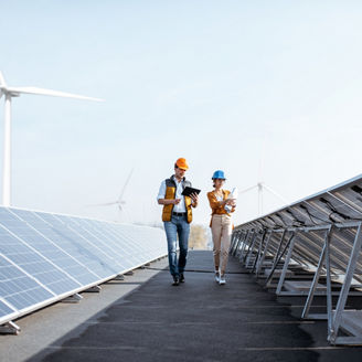 View on the rooftop solar power plant with two engineers walking and examining photovoltaic panels. Concept of alternative energy and its service
