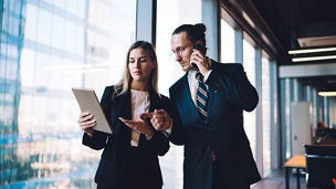 Caucasian boss reading financial news on modern touch pad while communicating with corporate investor via cellphone, formally dressed colleagues using technology with 4g internet in office interior