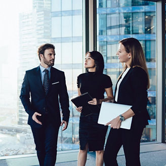 Prosperous male and female colleagues enjoying working together joking on friendly conversation, confident man manager talking to women colleagues dressed in formal elegant wear walking in office