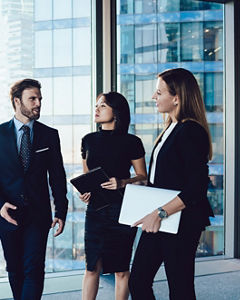 Prosperous male and female colleagues enjoying working together joking on friendly conversation, confident man manager talking to women colleagues dressed in formal elegant wear walking in office