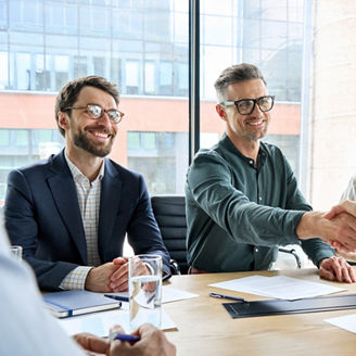 Happy businessman and businesswoman shaking hands at group board meeting. Professional business executive leaders making handshake agreement successful company trade partnership handshake concept.