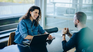 Smiling businesswoman taking interview of a job applicant. Friendly recruitment manager interviewing young man in office boardroom.