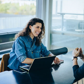 Smiling businesswoman taking interview of a job applicant. Friendly recruitment manager interviewing young man in office boardroom.