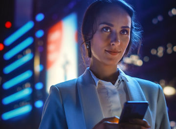 Beautiful Young Woman Using Smartphone Standing on the Night City Street Full of Neon Light. Portrait of Gorgeous Smiling Female Using Mobile Phone.