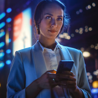 Beautiful Young Woman Using Smartphone Standing on the Night City Street Full of Neon Light. Portrait of Gorgeous Smiling Female Using Mobile Phone.