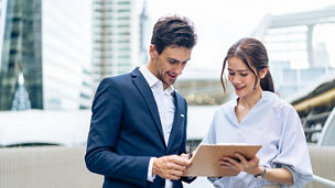Caucasian businessman and Asian woman worker walk outdoors in the city. Attractive young male and female employee people talking and plan brainstorm a project while walking outside to office company.