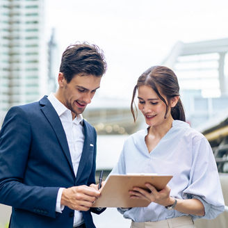 Caucasian businessman and Asian woman worker walk outdoors in the city. Attractive young male and female employee people talking and plan brainstorm a project while walking outside to office company.