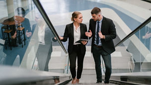 Two business people using tablet computer while going up the escalator.