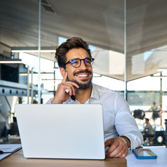 Happy Latin business man working at laptop in office looking away. Happy young businessman professional using computer sitting at desk thinking of corporate technology ai solutions. Copy space
