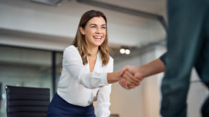 Happy mid aged business woman manager handshaking greeting client in office. Smiling female executive making successful deal with partner shaking hand at work standing at meeting table.
