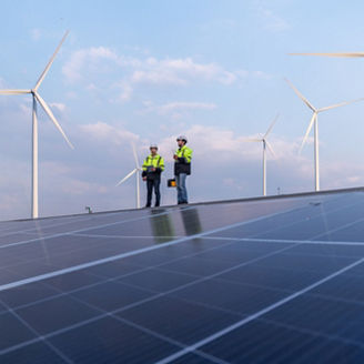 Engineers work walking on factory roof inspect survey and check solar cell panel by hold boxed with turbine wind mill field background is ecology energy alternative power factory concept.
