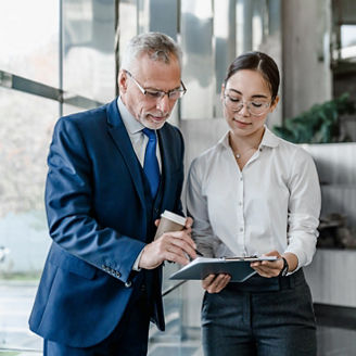 Two business people partners coworkers colleagues discussing about work at office stairs. Female workers manager showing document contract graphs and charts for her mature senior boss