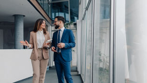 Two business professionals walking and discussing a project in a modern office, collaborating effectively amidst sleek architecture and expansive glass windows