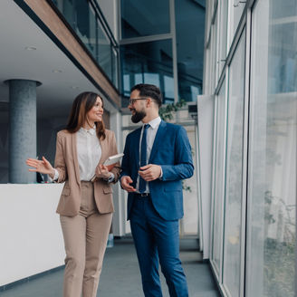 Two business professionals walking and discussing a project in a modern office, collaborating effectively amidst sleek architecture and expansive glass windows