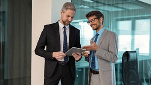Two business people discussing work together using a tablet in a modern office.