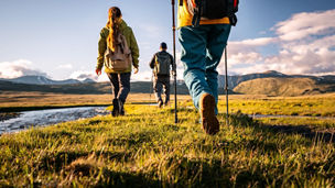 Close-up view of tourists walking along a mountain plateau towards a river in the rays of the setting sun, low angle view
