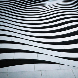 A professional architectural shot focusing on the repetitive, wave-like structure of a skyscraper's balconies. The high-contrast composition highlights the flowing white lines of the terraces against the dark shadows of the windows, creating a mesmerizing rhythmic pattern.