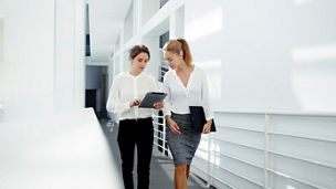 Two female managing directors discussing ideas of project on digital tablet while walking down in office hall, confident women entrepreneurs working on touch pad while going to the conference room 
