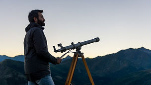 Man looking at mountain peaks near telescope in summer evening at sunset on mountain outdoor.