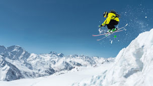 A skier in full sports equipment jumps into the precipice from the top of the glacier against the background of the blue sky and the Caucasian snow-capped mountains. Elbrus region. Russia
