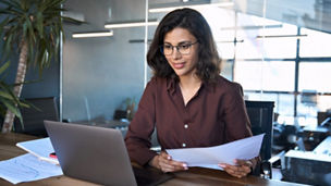 Focused latin hispanic young business woman working on laptop computer reading financial document report in office. Accountant entrepreneur manager businesswoman doing paperwork using pc. Copy space