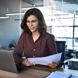 Focused latin hispanic young business woman working on laptop computer reading financial document report in office. Accountant entrepreneur manager businesswoman doing paperwork using pc. Copy space