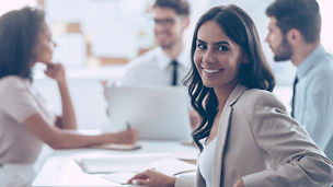 Beautiful cheerful woman looking at camera with smile while sitting at the office table with her coworkers