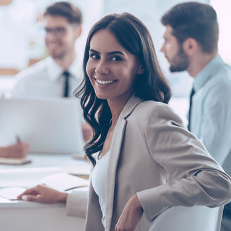 Beautiful cheerful woman looking at camera with smile while sitting at the office table with her coworkers