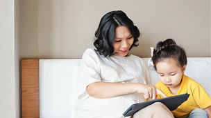 Smiling young mother showing educational application on tablet computer to her little daughter