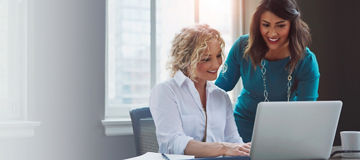 Business women, laptop and collaboration for public relations, digital campaign and planning in office. Smile, happy and banner with professional team with tech, meeting and conversation with mockup.