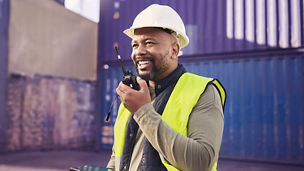 Logistics, radio and a black man in shipping container yard with tablet. Industrial cargo area, happy transport worker talking on walkie talkie in safety gear and working for global freight industry.; Shutterstock ID 2210454365; purchase_order: Advisory assurance marketing; job: anne ; client: AI Campagne