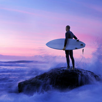 Surfer standing on rock with sea waves
