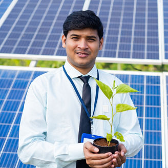 banker holding tree plant in hand in front of solar panel by looking at camera - concept of environmental growth, sustainable lifestyle and renewable energy.