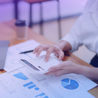 Frau sitzt an Schreibtisch mit Taschenrechner in der Hand