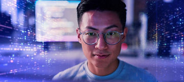 Close-up of a man wearing round glasses, facing forward, with blurred blue and purple digital light patterns and interface elements in the background