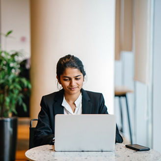 A wonderful Indian lady sitting inside a cafeteria while working. She is smiling in front of a laptop while discussing with a teammate. 