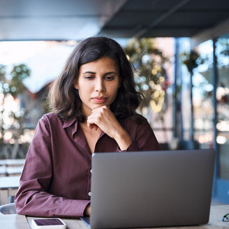 Thoughtful serious freelance entrepreneur business woman working on laptop computer remotely outdoors. Thinking focused busy latin, middle eastern indian young female worker using pc for study, work