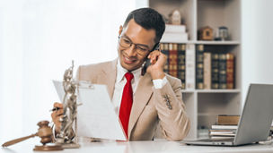 Middle-aged Asian indian people male lawyer meticulously reviews legal documents. Courtroom judge hammer and goddess scales. Depicting the essence of legal counseling and comprehensive services.