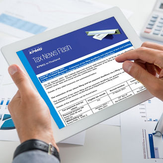 Hands holding a tablet displaying a tax news update, with financial charts, documents, and a calculator on a desk