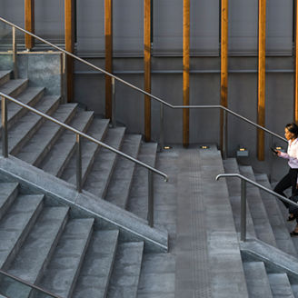 A woman in a white shirt and black pants with a black handbag walking upstairs while looking down at the phone