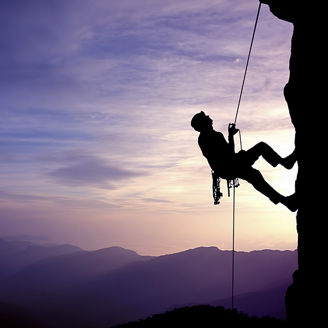 Eine Person klettert an einer Felswand bei Sonnenuntergang, während der Himmel in violetten und blauen Tönen leuchtet.