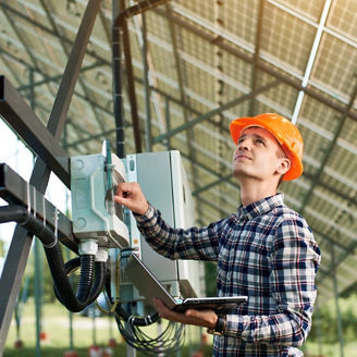Technician inspecting electrical equipment beneath a solar panel installation.