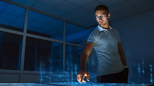   A person pointing at data on a screen in a dark room with windows