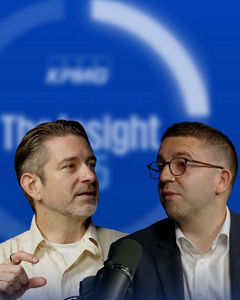 Two speakers in conversation beside a microphone against a blue background with blurred circular text